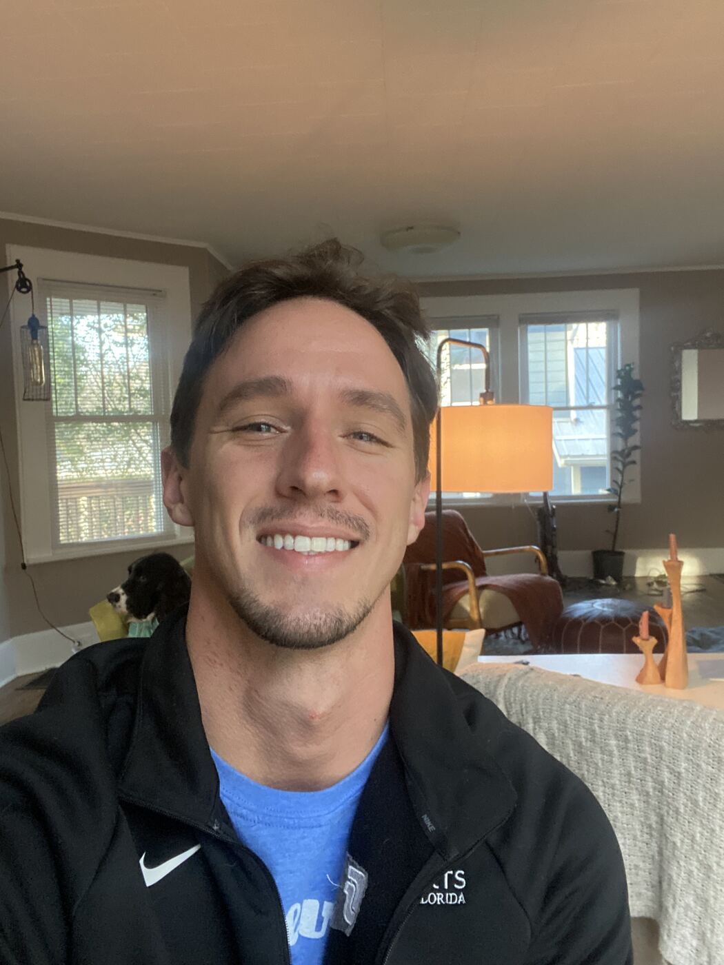 Dylan Lennon on move-in day at his first West Asheville home, wearing a Florida jacket, with his dog Wesley in the background